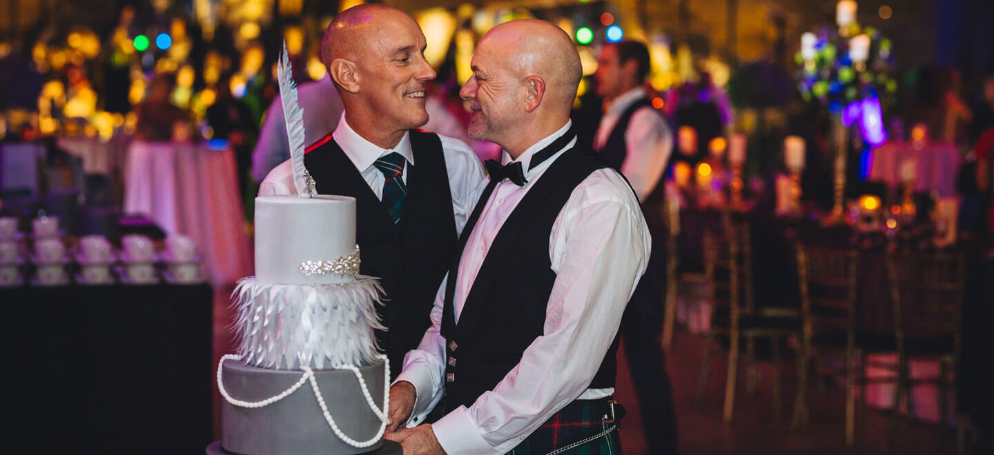 Gay grooms cut their cake in Dry Berth of the unique wedding venue Cutty Sark wedding venue via the Gay Wedding Guide 9