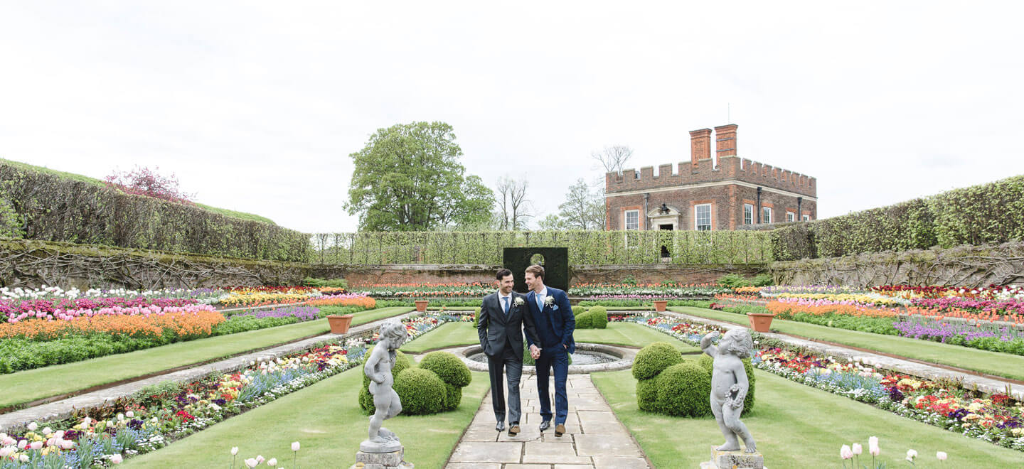 Gay grooms walk through pond garden at Hampton Court Palace unique royal wedding venue surrey gay palace wedding guide 9