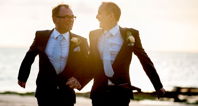 Guy and Andrew walk hand in hand on margate bay after their same sex wedding at the Turner Contemporary Margate 3 5
