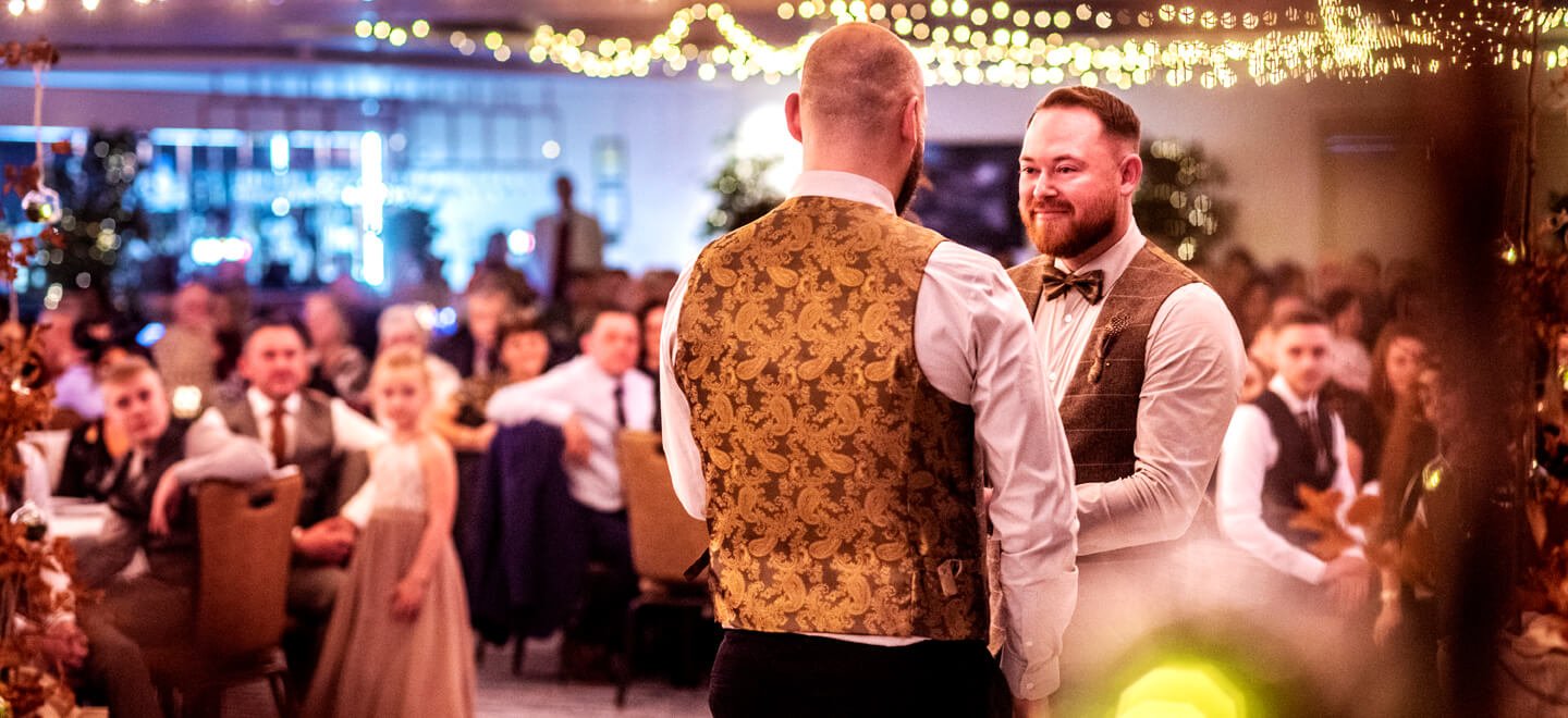 two gay grooms holding hands and dancing at their wedding while people watching at oec in sheffield via gay wedding guide 9