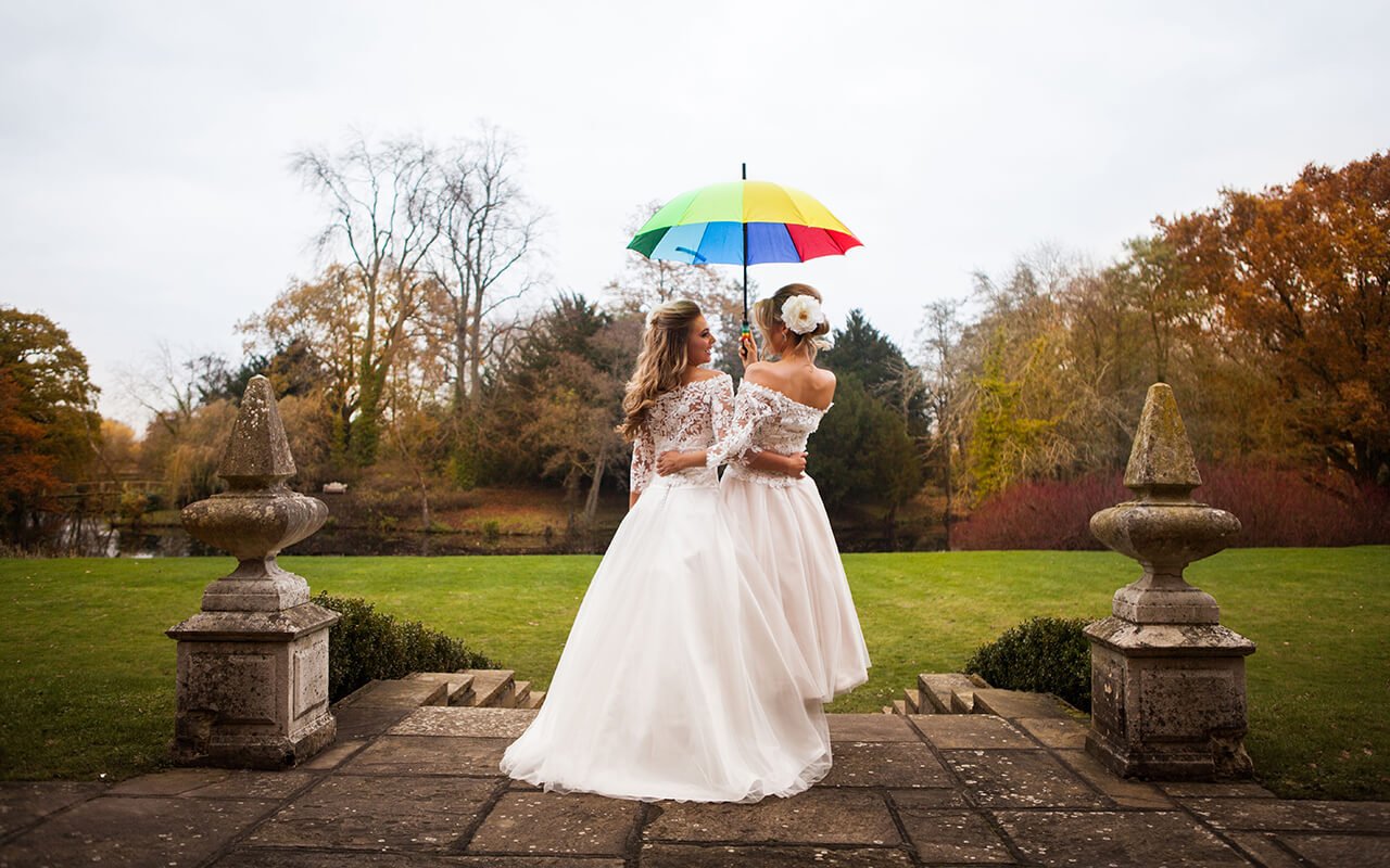 two lesbian brides staying in the rain under multicoloured umbrella 9