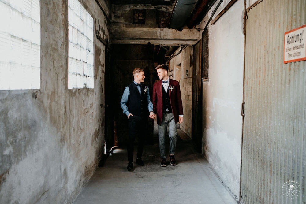 Grooms hold hands at styled gay wedding shoot at Germany fabric factory.1 Image by JuliaBartelt 1 5