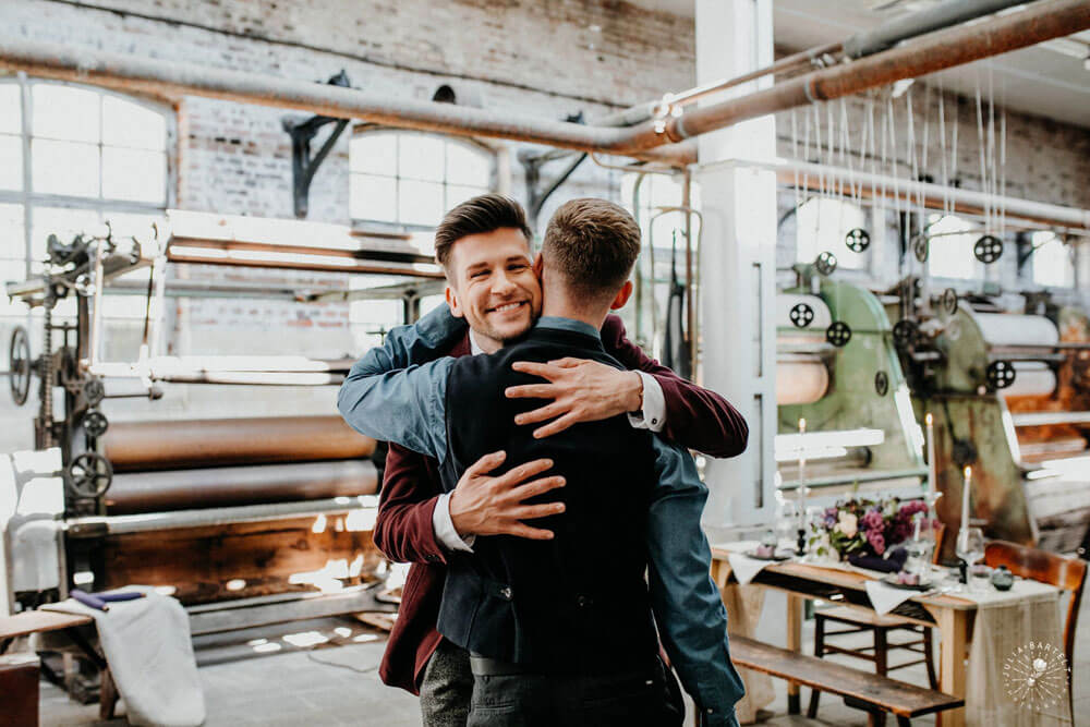 Grooms hug at styled gay wedding shoot at Germany fabric factory.1 Image by JuliaBartelt 1 5
