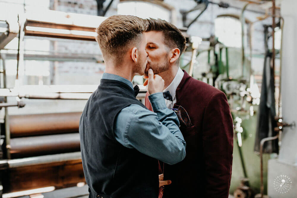 Grooms lean in and kss at styeld gay wedding shoot at Germany fabric factory.1 Image by JuliaBartelt 1 5