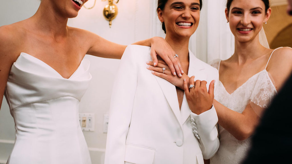 Three brides wearing lesbian wedding suits talking with someone